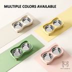 Four pet double bowls shown in different colors: cream, pale yellow, mint green, and blush pink, each with stainless steel bowls and small wooden feet. The text 'MULTIPLE COLORS AVAILABLE' appears at the top, and the brand name 'PET MANYA' is shown at the bottom right.