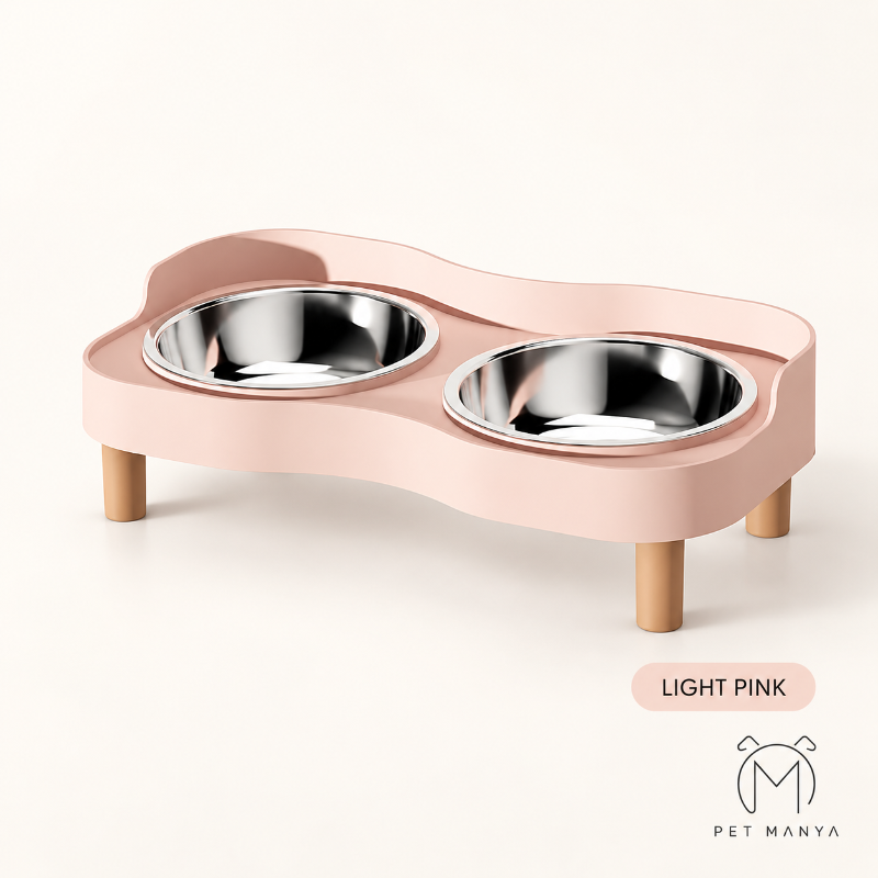 A light pink elevated pet feeding station with two stainless steel bowls and four wooden legs, shown on a clean off-white background with a 'LIGHT PINK' label and the 'PET MANYA' logo.