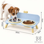 A small dog stands beside a light blue elevated pet feeder with two stainless steel bowls, one containing dry food. White background with dimension lines showing 32cm width, 15cm height, 6.