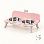 A pink elevated pet feeder and water bowl stand with two stainless steel bowls, shown on a clean off-white background. The brand logo 'PET MANYA' is visible in the bottom right corner.