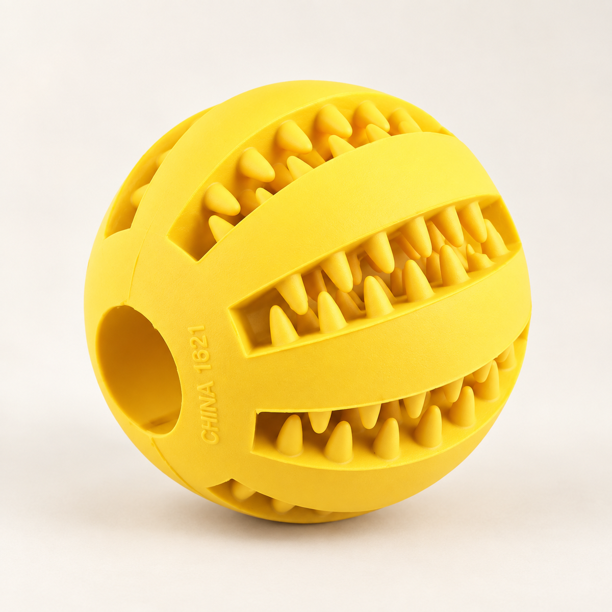 A bright yellow silicone dog toy ball with a textured, tooth-like pattern on its surface, photographed on a clean white background.
