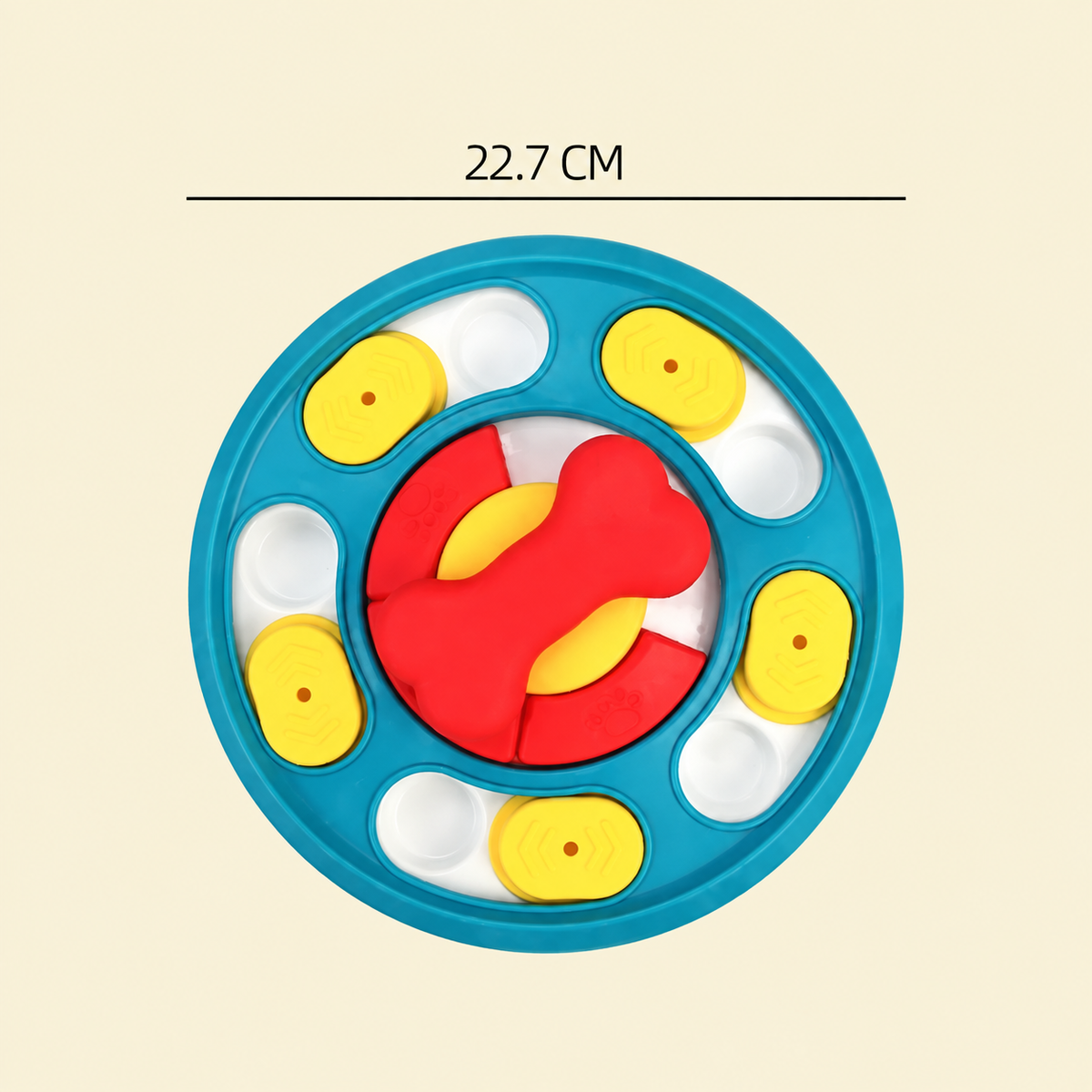 A colorful circular toy or puzzle with a blue outer ring, red and yellow central pieces, and several small white oval compartments, shown on a light beige background with a measurement line reading 22.7 CM above it.