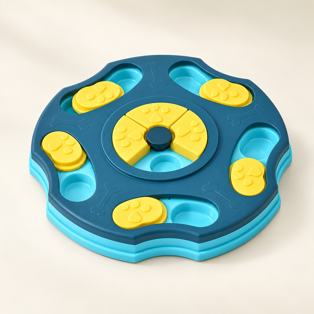 A circular dog puzzle toy with a dark blue outer ring, light blue raised edges, and bright yellow interactive pieces including paw-print-shaped covers and a central wheel, photographed on a clean off-white background.