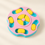 A colorful plastic toy puzzle board with a pink outer ring, turquoise blue base and slots, and yellow movable pieces, photographed on a clean light beige background.