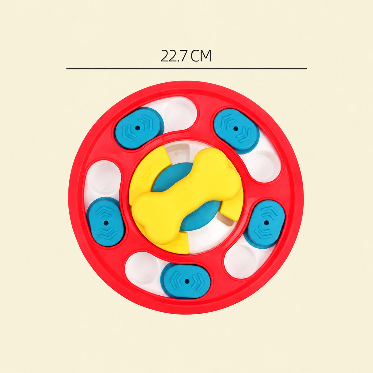 A colorful circular dog toy with a red outer ring, blue textured discs, a yellow bone-shaped center piece, and white oval cutouts, shown on a light beige background with a measurement label reading 22.7 CM above.