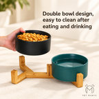 A pet double bowl set with a black food bowl held by a hand, a teal water bowl on a bamboo stand, and text reading 'Double bowl design, easy to clean after eating and drinking.'.